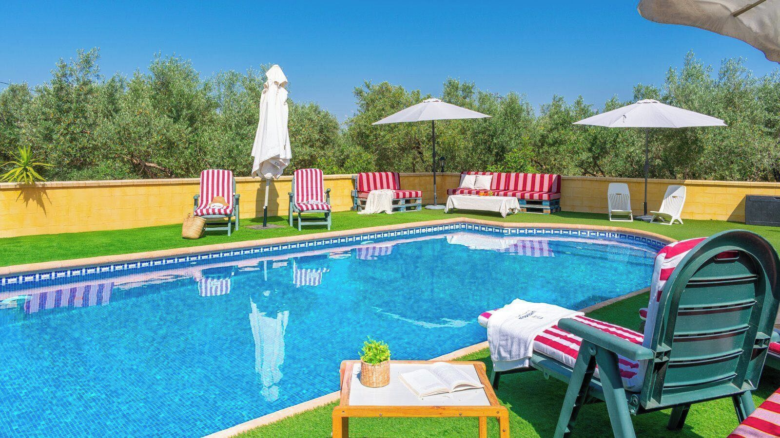Una piscina con lettini e ombrelloni, circondata dal verde.