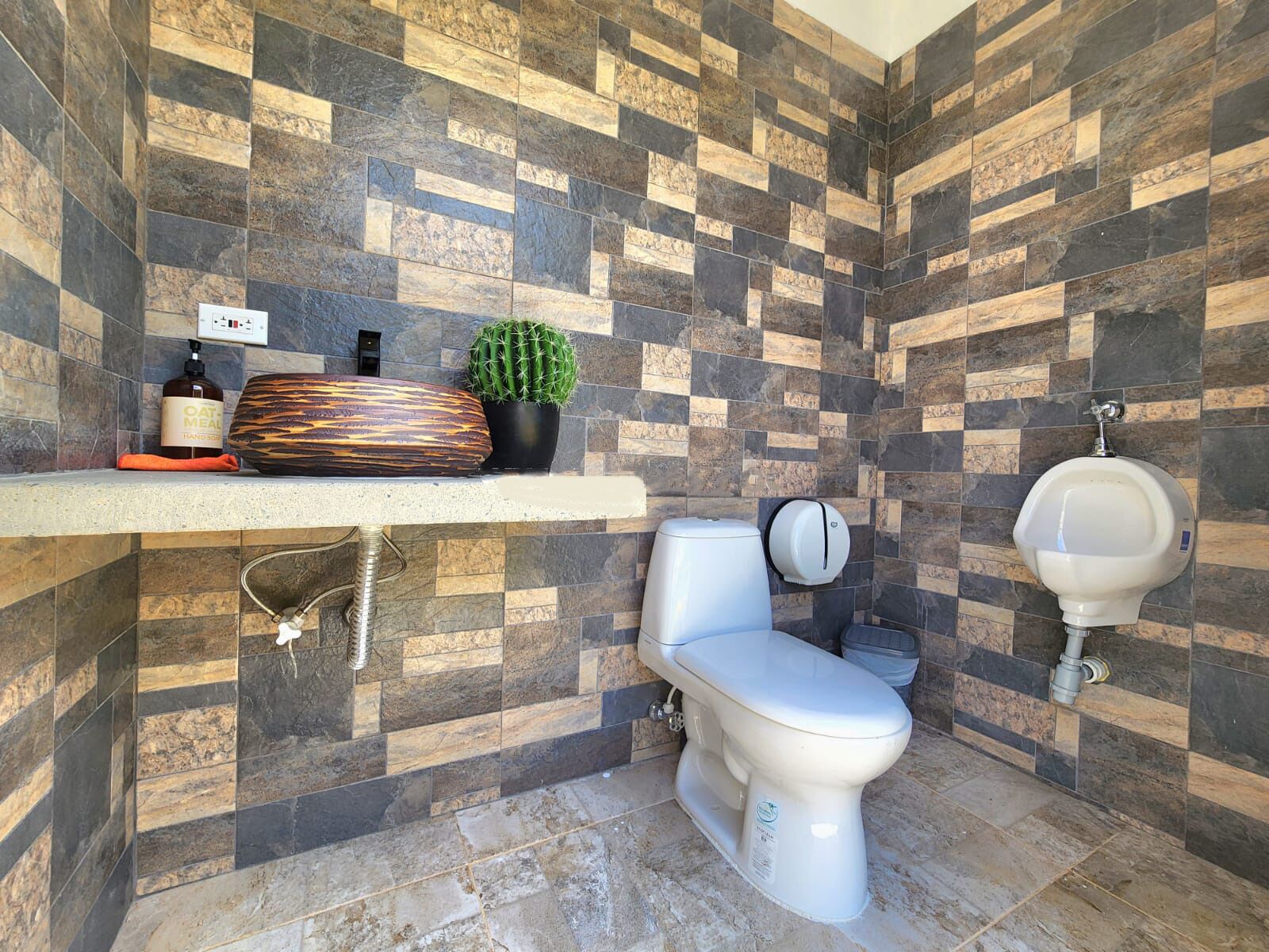 Une salle de bain avec un mur carrelé, des toilettes, un lavabo et un urinoir.
