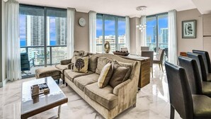 A modern living room with a sofa, coffee table, and chairs, large windows with city views, and a dining area. - Spacious Clermont Villa Sleeps 16 Pool (Hallandale Beach)