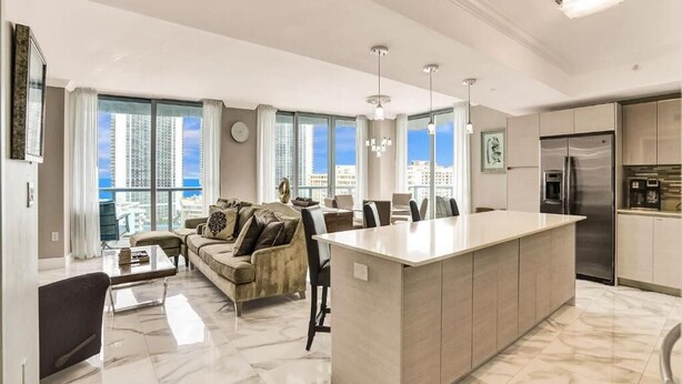A modern kitchen with a central island, a dining area with a sofa, and large windows offering a city view. - Spacious Clermont Villa Sleeps 16 Pool (Hallandale Beach)