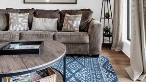 A modern living room with a grey sofa, a round coffee table, a patterned rug, a floor lamp, and a large window with curtains. - Golf View, 2 porches, 3 pools, Hot Tub, Resort! (Branson)