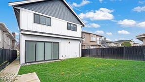 A two-story house with a large sliding glass door, a fenced backyard, and a clear blue sky. - Modern 3BR Gem | Close to Transit | 15m to DT (Vancouver)