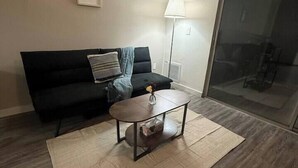 Una sala de estar con un sofá negro, una mesa de centro, una lámpara y un amplio ventanal.