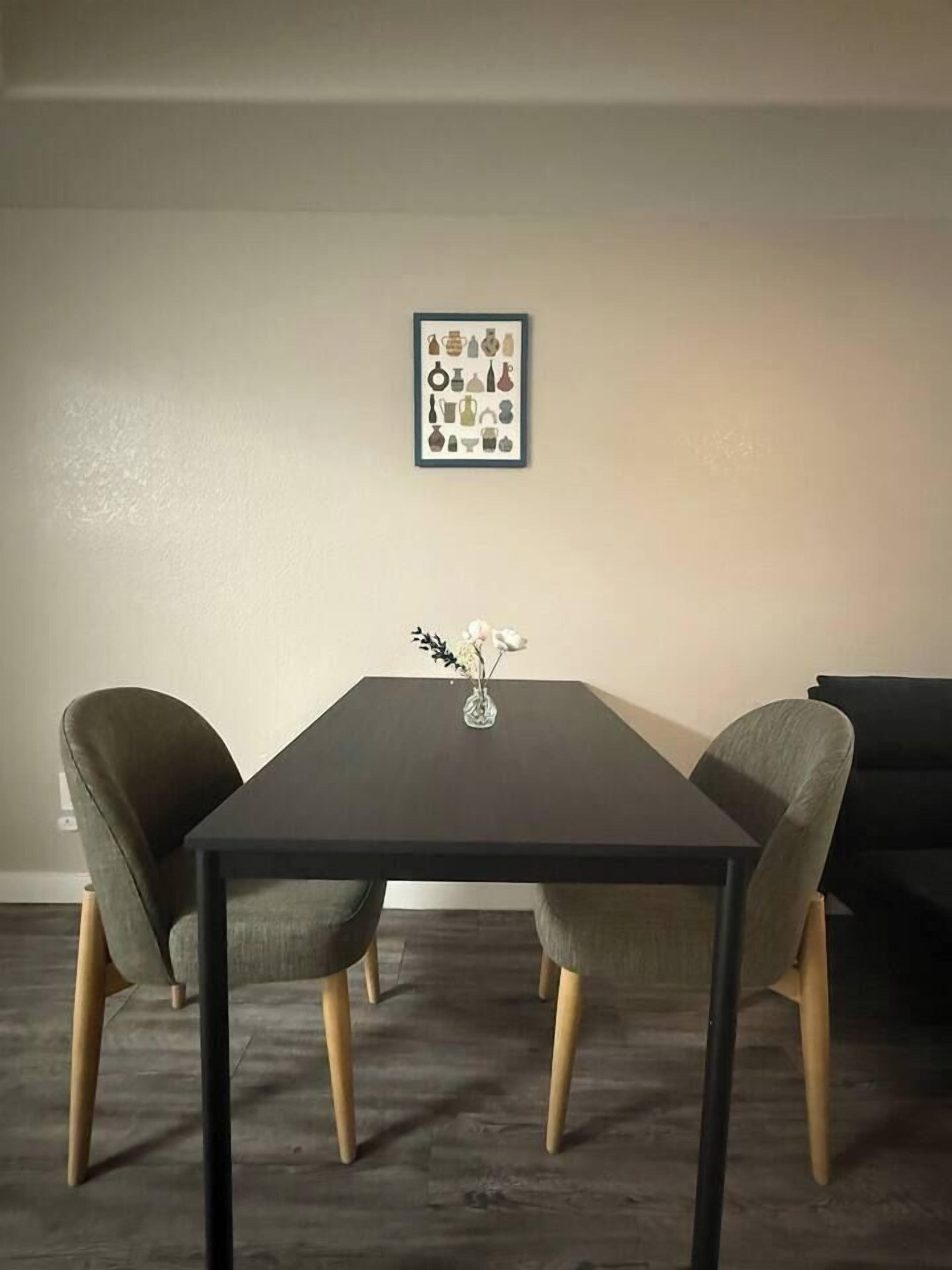 A dining table with two chairs, a vase with flowers, and a framed picture on the wall.