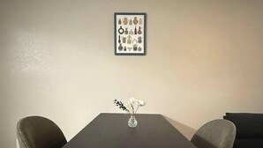 Una mesa de comedor con dos sillas, un florero con flores y un cuadro en la pared.