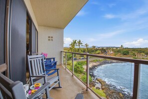 A balcony with a view of the ocean, a chair, and a table with food. - Kuhio Shores 407 (Koloa)