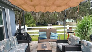 Un patio al aire libre con mobiliario de mimbre, una parrilla y una zona techada con luces colgantes.