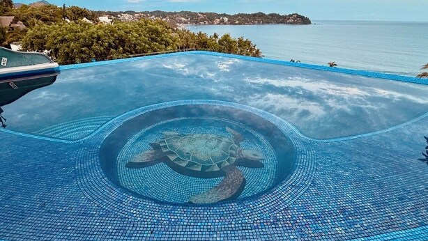 En pool med et skildpaddedesign på gulvet, omgivet af havudsigt og en fjerndliggende ø.