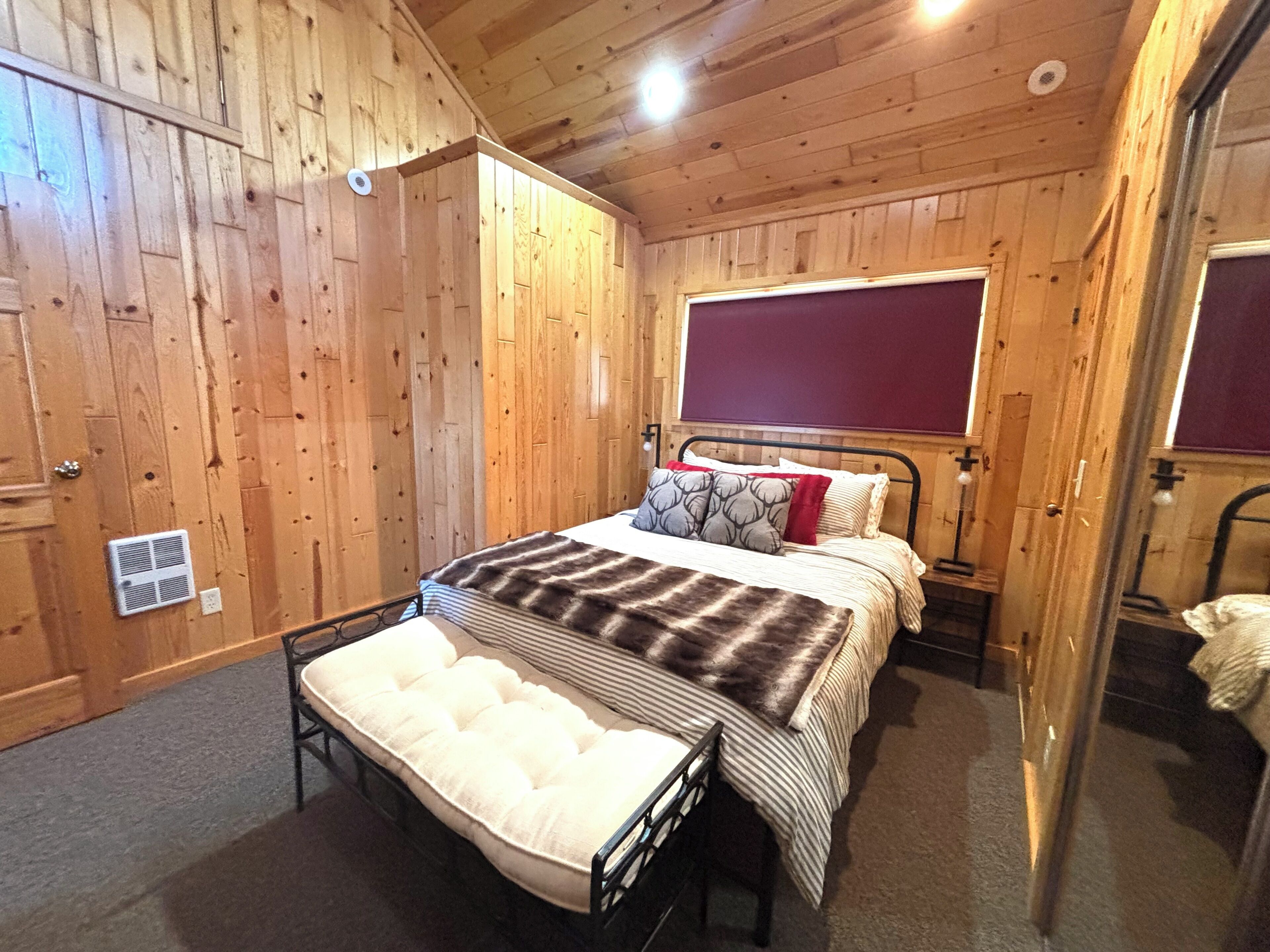 A wooden-paneled room with a bed, a bench, and a window.