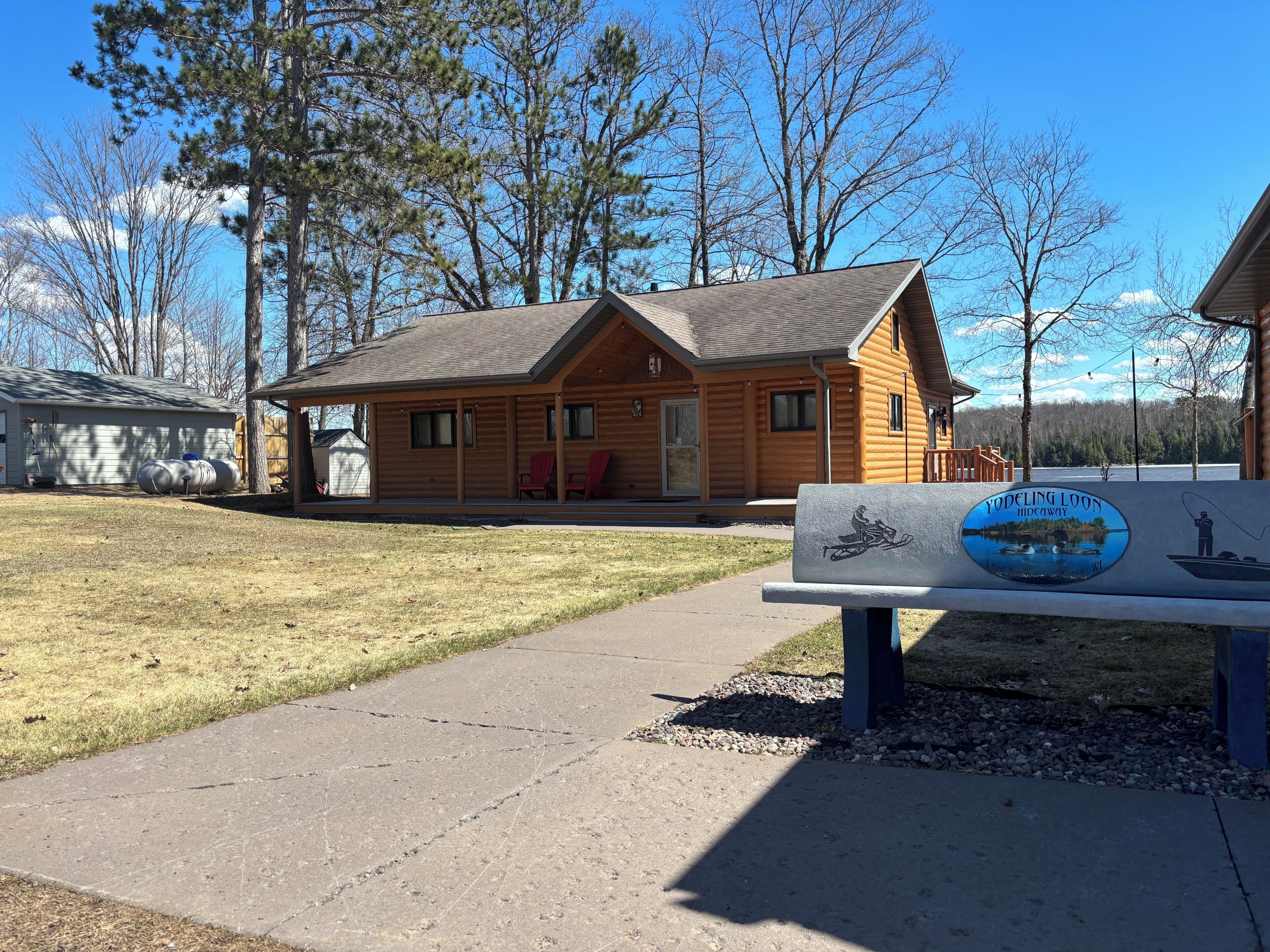 A wooden cabin with a porch, a bench with a sign, and a clear sky.