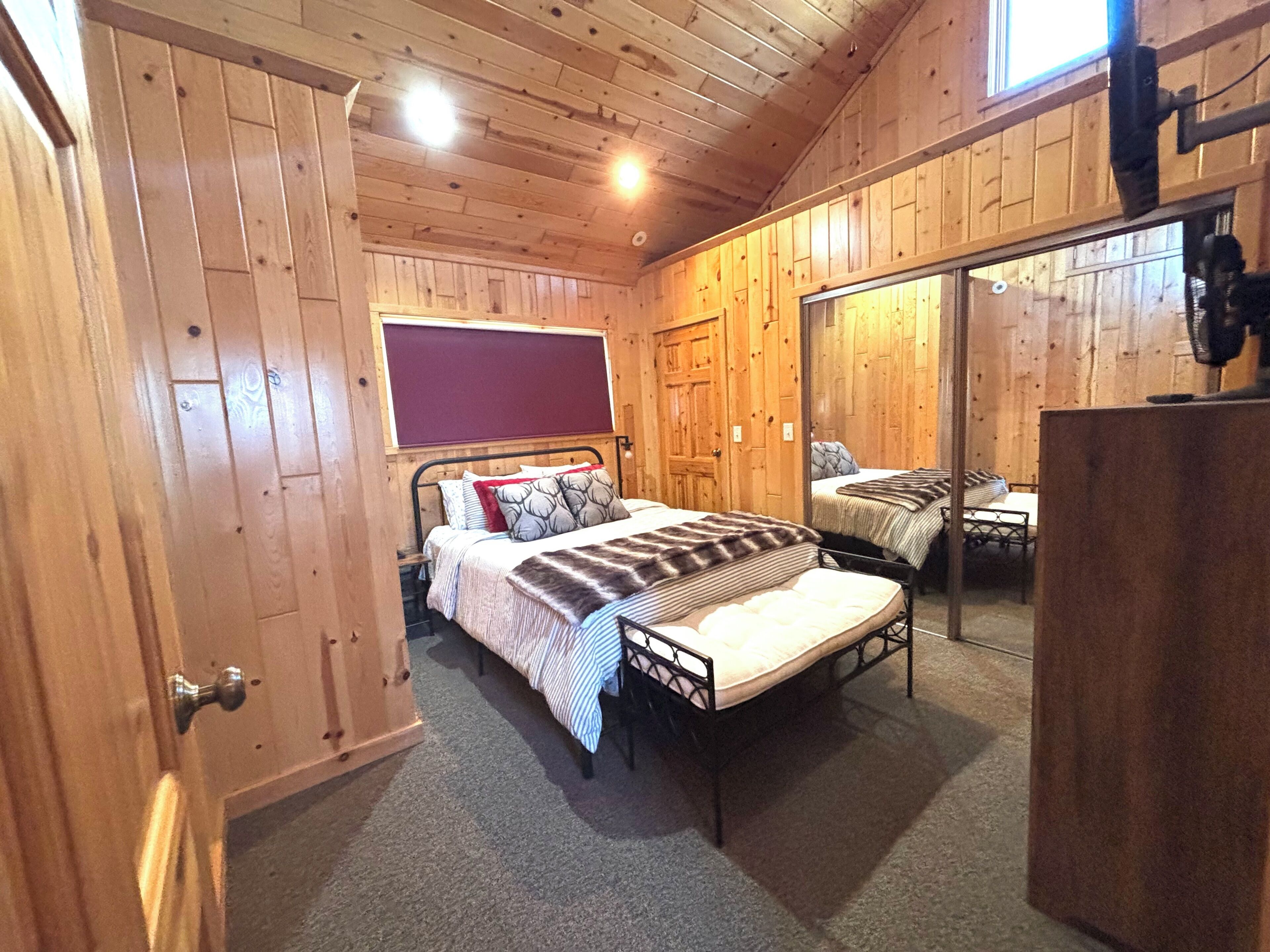 A wooden-paneled room with a bed, a mirror, and a small table.