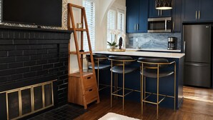 A modern kitchen with dark blue cabinets, a black refrigerator, a wooden ladder, and a bar area with stools. - The Emerald Cottage/Main Street/Garage (Deadwood)