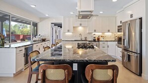 Una cocina moderna con una isla central, electrodomésticos de acero inoxidable y un amplio ventanal con vistas a un jardín.