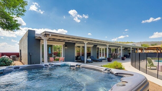 Un área de piscina moderna al aire libre con un jacuzzi, sillas de descanso y un porche cubierto.