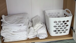 Une pièce avec un lit, une pile de serviettes pliées et un panier à linge blanc.