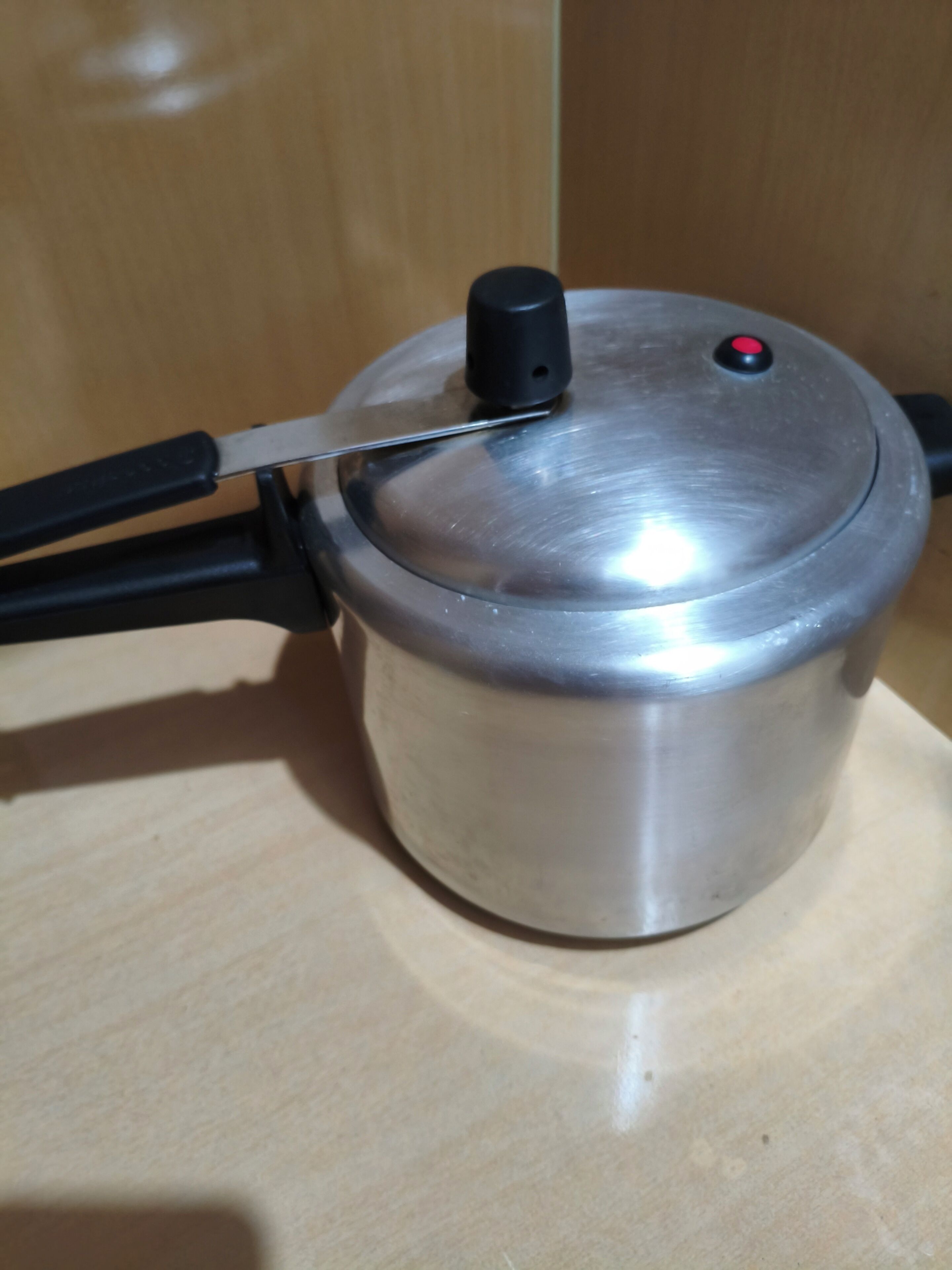 Ein Edelstahl-Topf mit Deckel und schwarzem Griff auf einer Holzoberfläche.