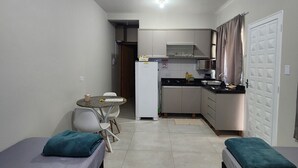 Una habitación compacta con dos camas, un pequeño kitchenette, una mesa de comedor y una puerta blanca.
