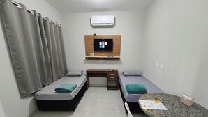 Una habitación pequeña y limpia con dos camas individuales, un escritorio, una silla, una mesa y un televisor fijado a la pared.
