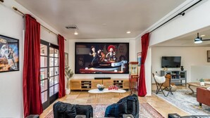 Ein Wohnzimmer mit großem Flachbildfernseher, Ledersofas, einem Couchtisch und einem Essbereich mit Tisch und Stühlen.
