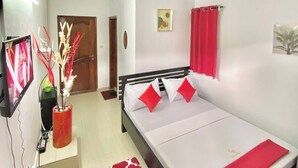 A bedroom with a bed, a TV, a red vase, and a red rug.