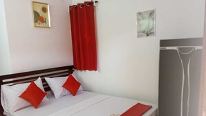 A bed with white bedding and red accents, a red curtain, and a gray wardrobe.