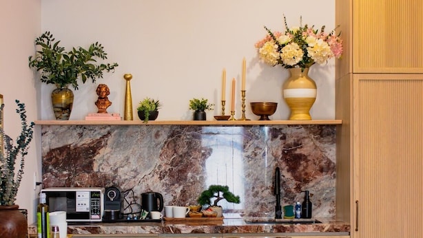 A kitchen with a marble backsplash, wooden cabinets, a microwave, and a dining area with chairs.