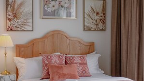 A neatly made bed with a wooden headboard, white bedding, and decorative pillows. There are framed floral artworks on the wall above the bed.