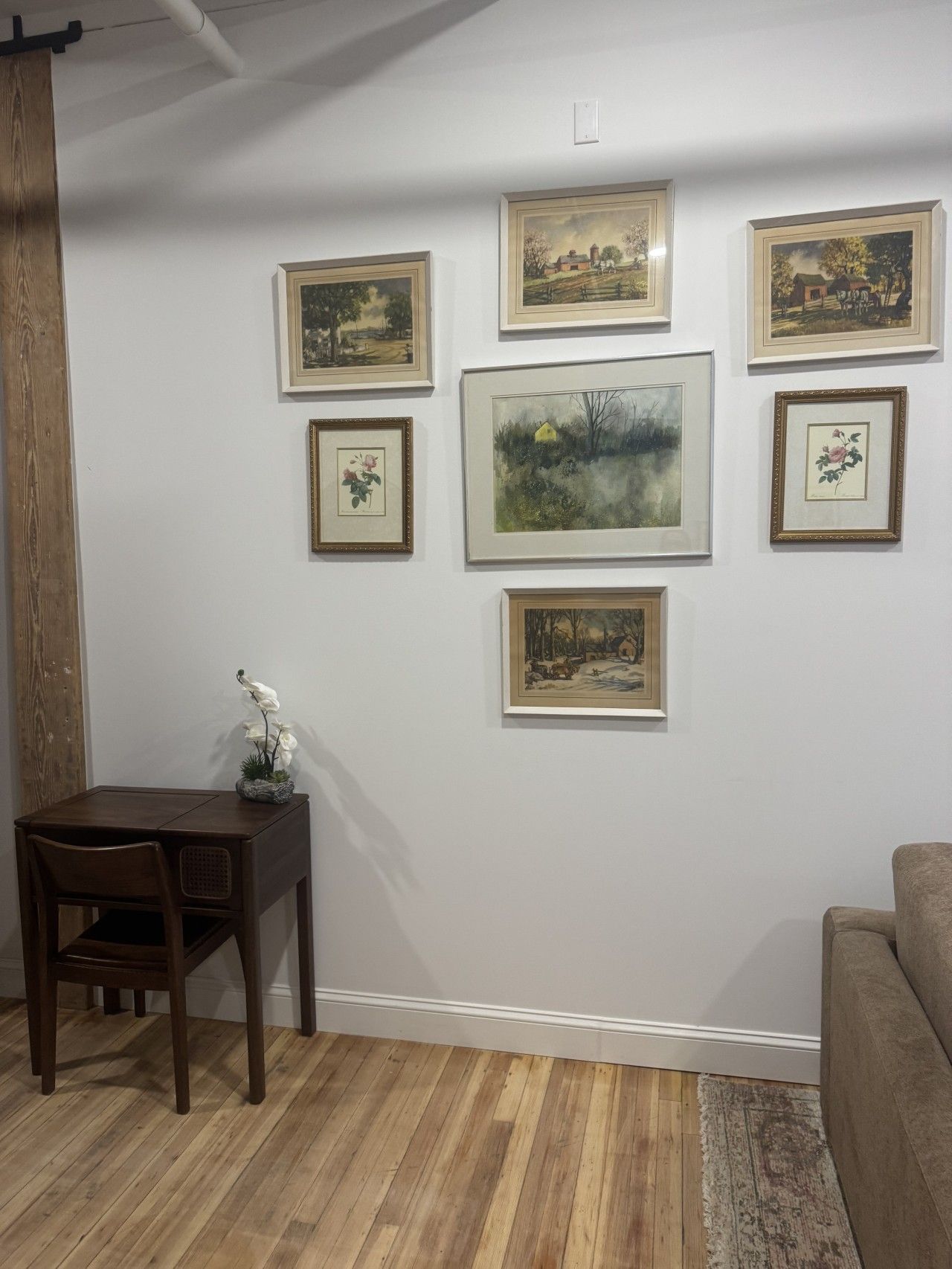 A room with a wooden floor, a dining table with chairs, a sofa, and several framed artworks on the wall.