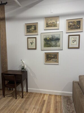 A room with a wooden floor, a dining table with chairs, a sofa, and several framed artworks on the wall.
