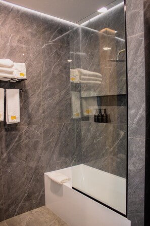 A modern bathroom with a glass-enclosed shower, a white bathtub, and neatly folded towels on a shelf.