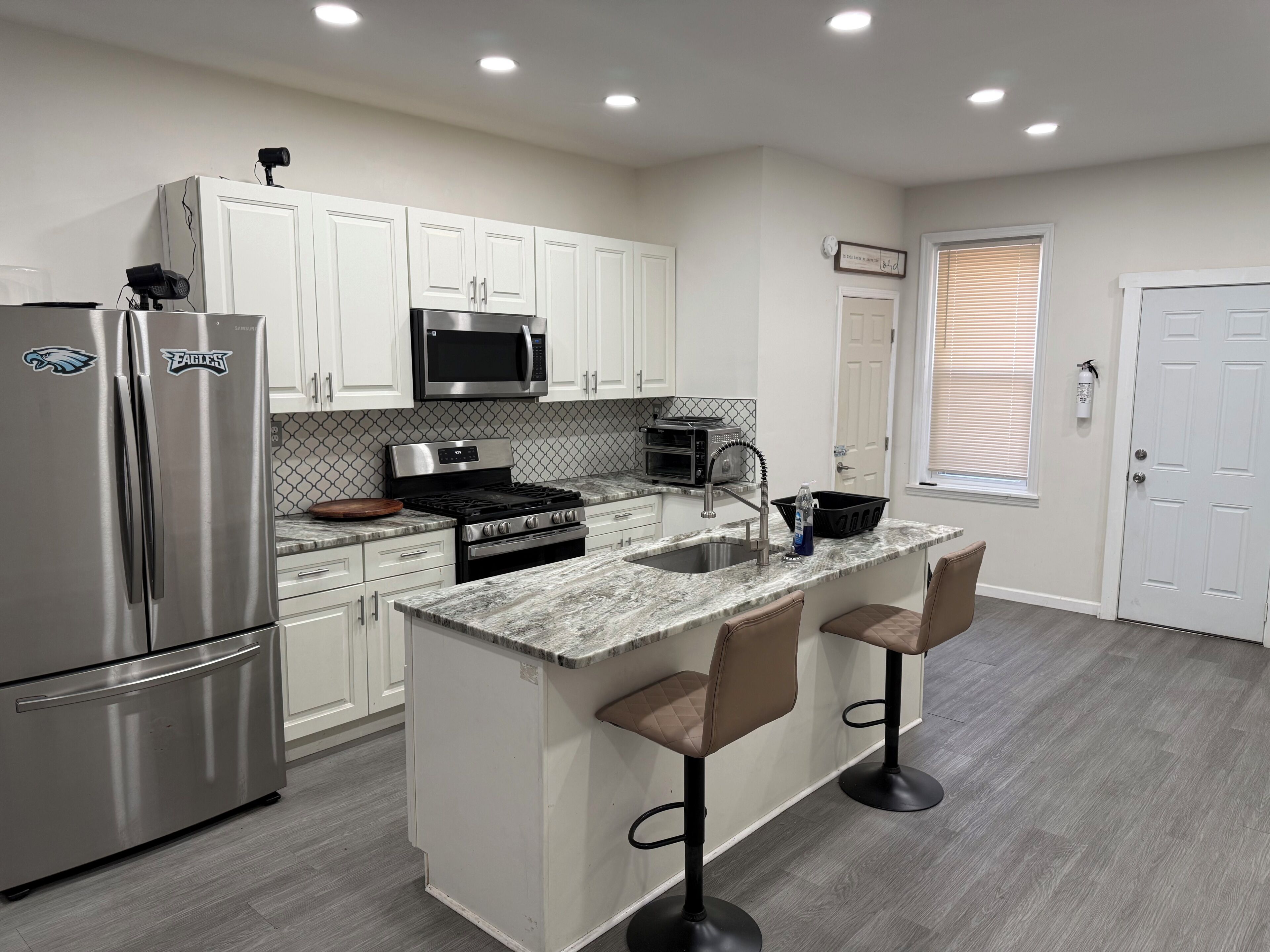 A modern kitchen with white cabinets, stainless steel appliances, a granite countertop, and two bar stools.