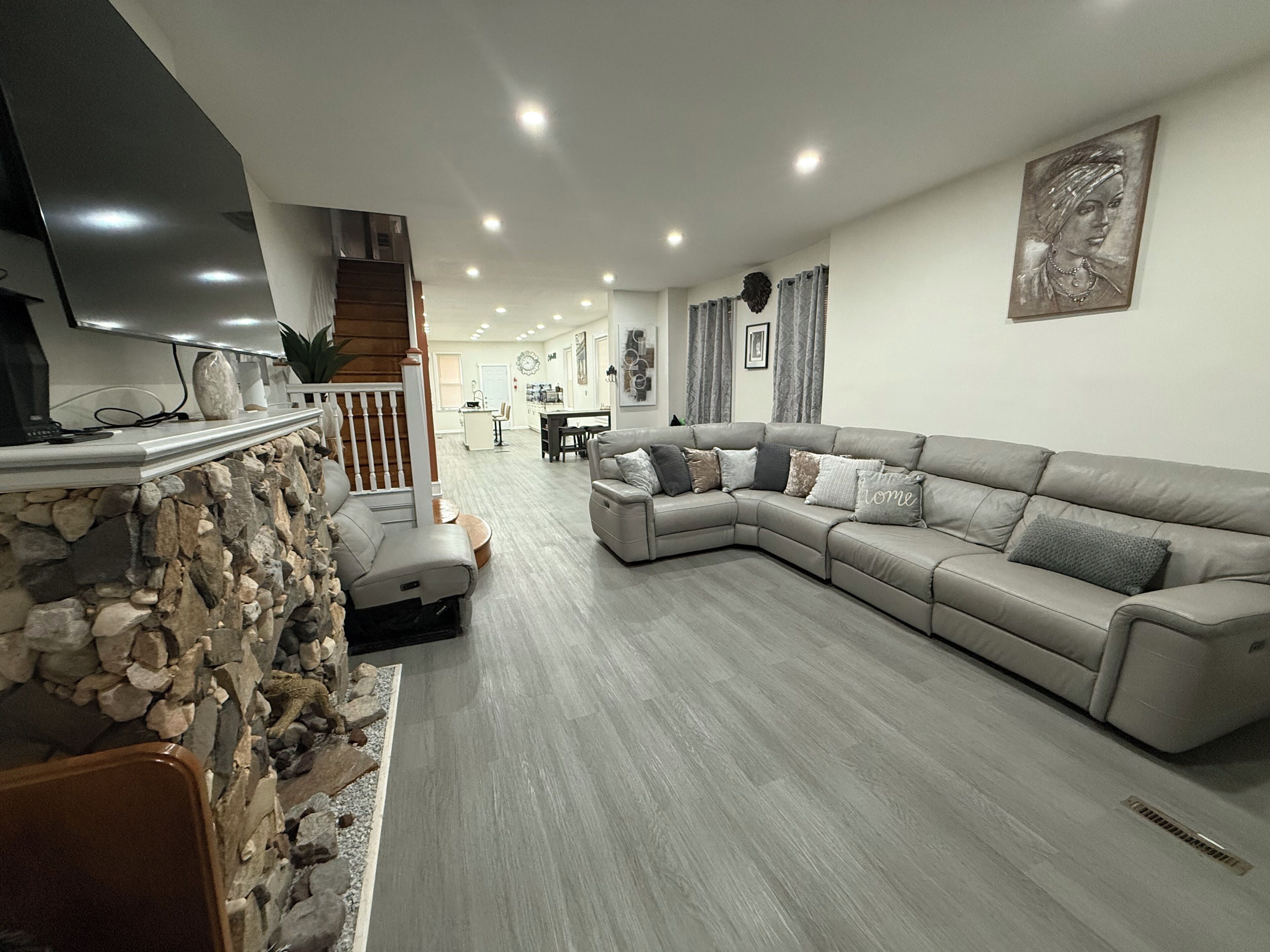 A modern living room with a stone fireplace, a grey sectional sofa, and a flat-screen TV mounted on the wall.