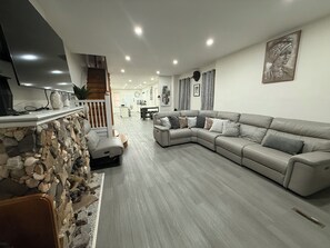 Uma sala de estar moderna com lareira de pedra, sofá modular cinza e televisão de tela plana na parede.