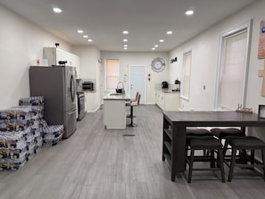 Een moderne keuken met een koelkast, oven en magnetron. Er is een eethoek met een tafel en stoelen.