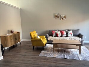 A living room with a sofa, yellow armchair, wooden cabinet, and two wall-mounted pictures. - Cozy Townhome close to airport, shopping, Toyota Music Factory and restaurants (Irving)