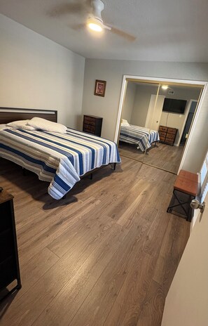 Ein Schlafzimmer mit Bett, Deckenventilator, Holzboden, Kommode und Spiegel, der den Raum reflektiert.