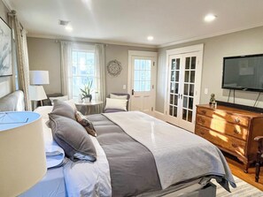 A bedroom with a large bed, bedside tables, a dresser, a TV, and a window with curtains. - Historic home near beaches & Newport, walk to town (East Greenwich)