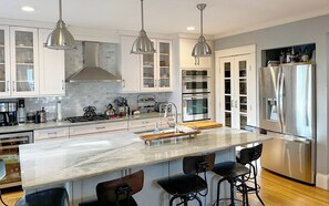 A modern kitchen with a central island, stainless steel appliances, and bar stools. - Historic home near beaches & Newport, walk to town (East Greenwich)