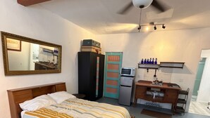 Een slaapkamer met een bed, een plafondventilator, een magnetron, een kast en een kleine kitchenette.