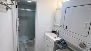 Een kleine badkamer met een ingebouwde wasmachine, een klein wastafeltje en een handdoekhouder.