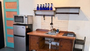 Een kleine keuken met een magnetron, koelkast, houten kast, spoelbak en een klein plankje met blauwe vazen.