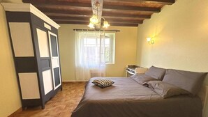 Un dormitorio con cama, piso de madera, armario, ventana con cortinas e iluminación empotrada en la pared.