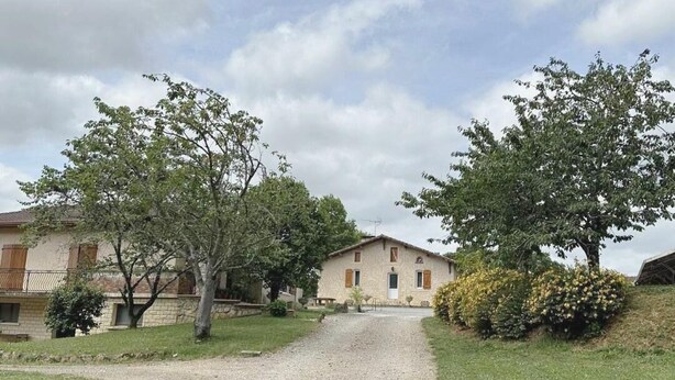 Una casa de campo con entrada de grava, rodeada de árboles y césped.