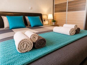 Ein Hotelzimmer mit einem Bett, einer türkisblauen Tagesdecke und aufgerollten Handtüchern.