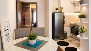 Une cuisine compacte équipée d’un réfrigérateur, d’un four et d’un four à micro-ondes. On y trouve un coin repas avec une table et des chaises, ainsi qu’une petite plante en pot posée sur la table.