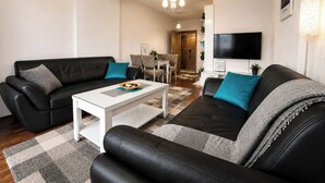 Un salon moderne avec un canapé en cuir noir, une table basse blanche et un téléviseur fixé au mur.