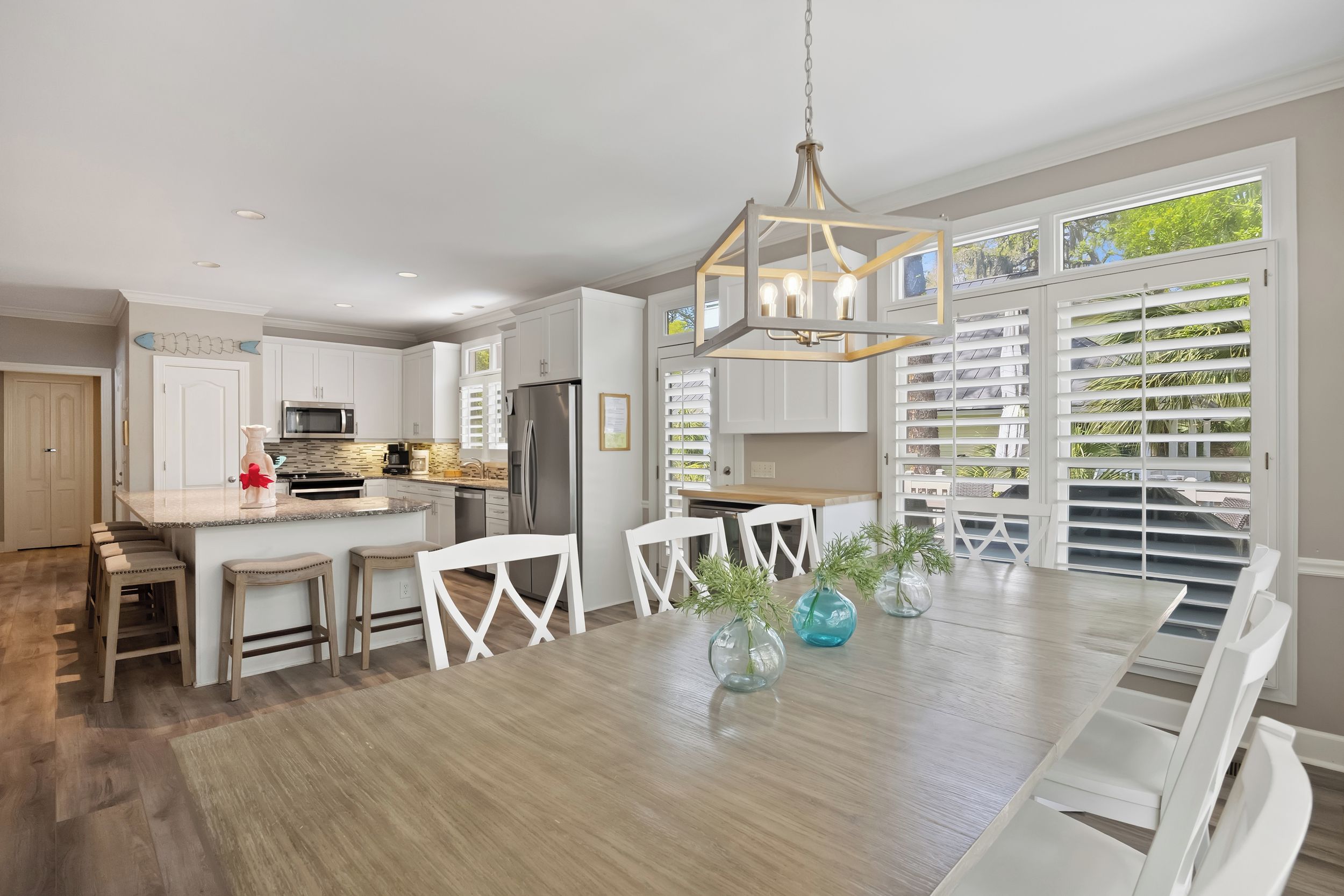 A modern kitchen with white cabinetry, a central island, and a dining area with a wooden table and chairs.