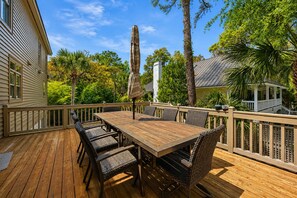 Eine Holzterrasse mit Tisch und Stühlen, umgeben von einem Geländer, mit Bäumen im Hintergrund.