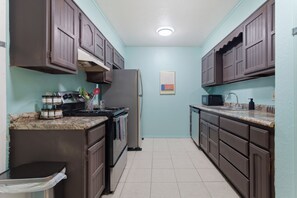 A kitchen with dark wooden cabinets, a stainless steel refrigerator, and a granite countertop. - Pastel Place | Colorful 3BR Tulsa Duplex (Tulsa)