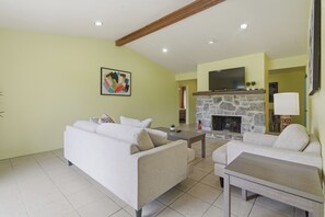 A living room with two sofas, a stone fireplace, a flat-screen TV, and a tiled floor. - Pastel Place | Colorful 3BR Tulsa Duplex (Tulsa)